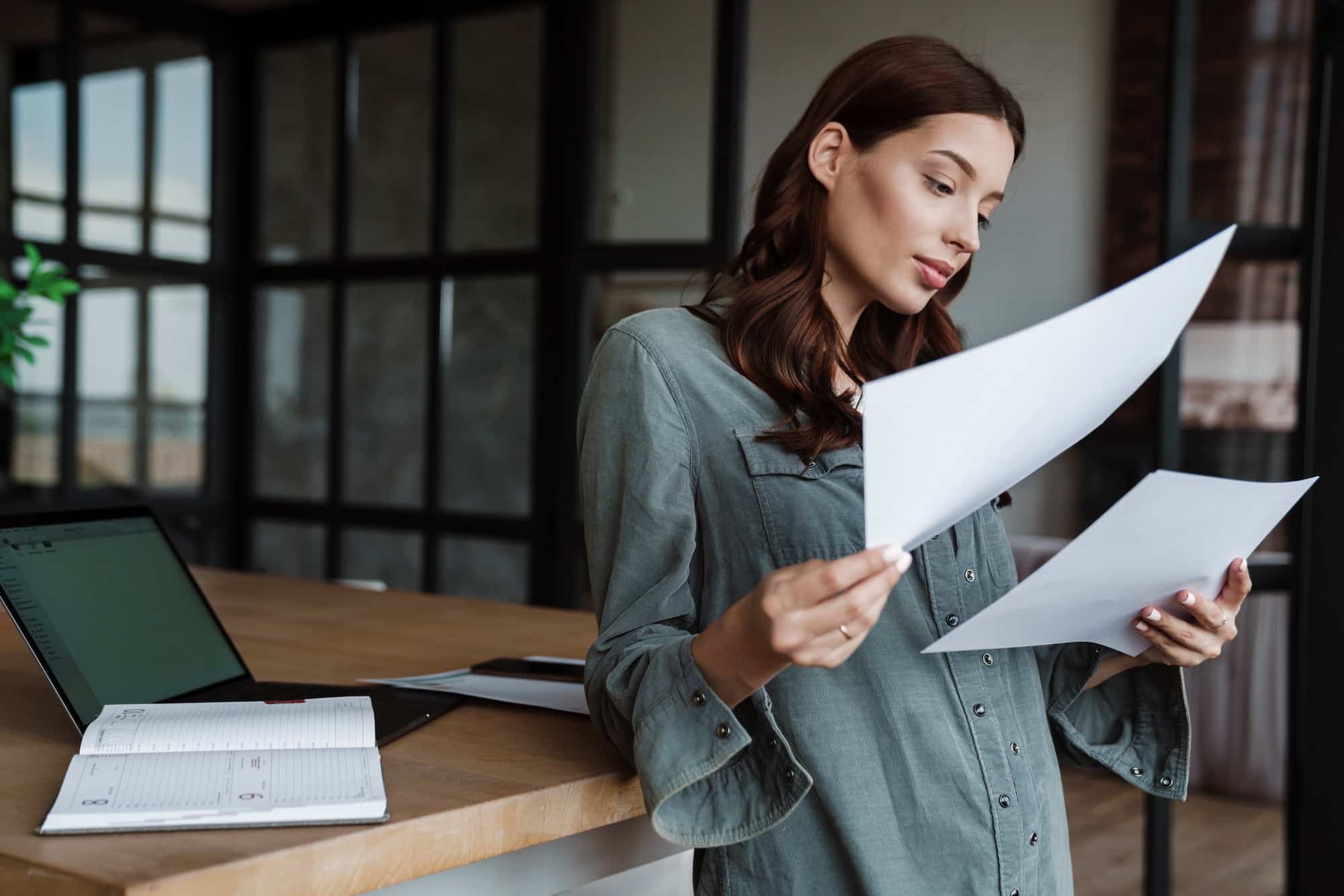 Beautiful focused woman working with papers and laptop